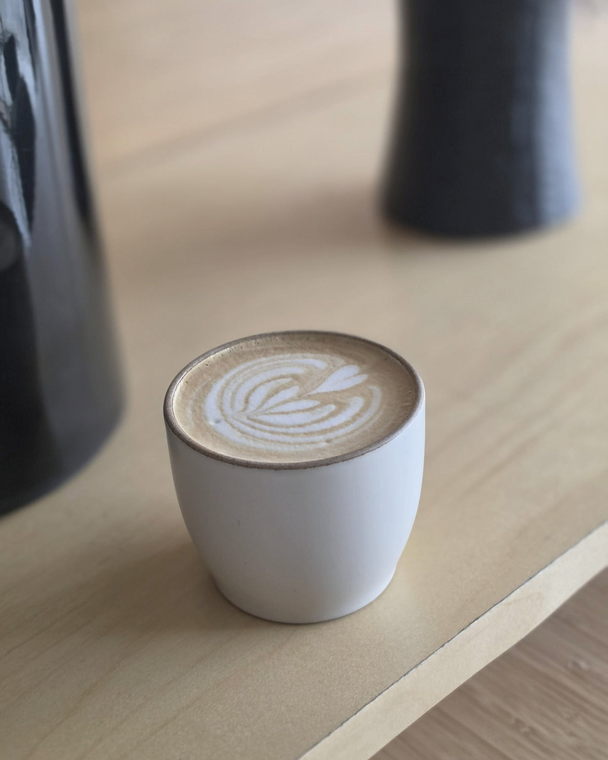 Latte in a white ceramic cup on a light wood counter